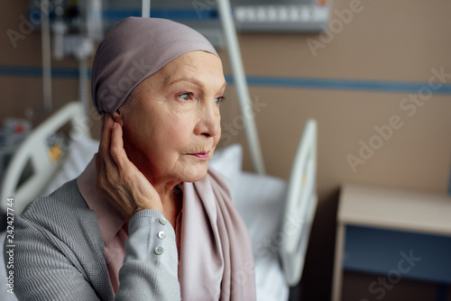 upset senior woman with cancer sitting on bed in hospital photo