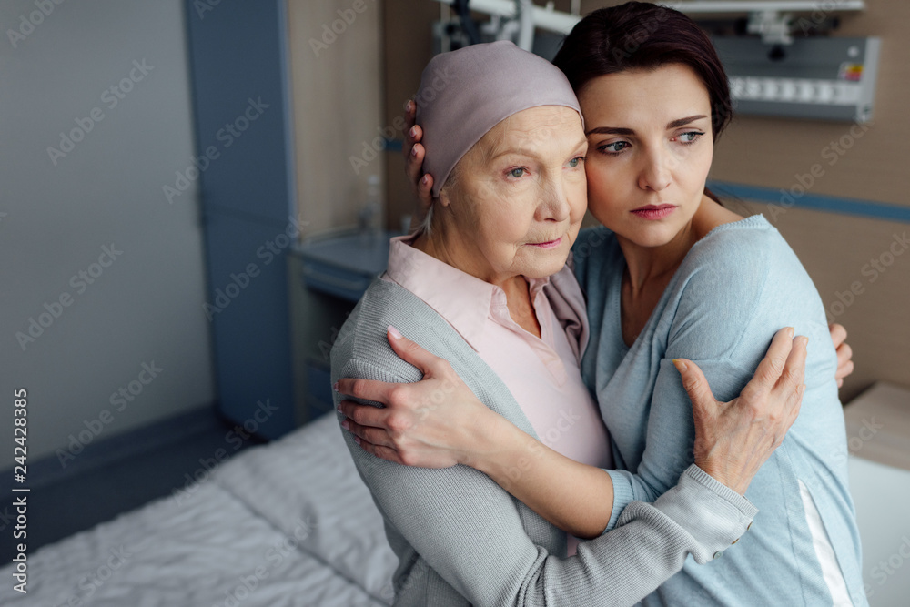 Fototapeta premium sad daughter embracing sick senior mother with cancer in hospital