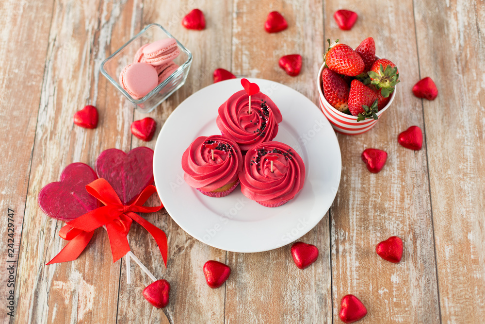 valentines day and sweets concept - close up of frosted cupcakes, red heart shaped chocolate candies, lollipops, macarons and strawberries valentines day and sweets concept - close up of frosted cupcakes, red heart shaped chocolate candies, lollipops, macarons and strawberries
