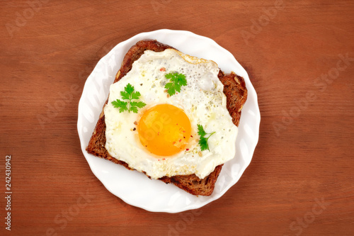 An egg cooked sunny side up on a toast, shot from the top on a rustic wooden background with copy space