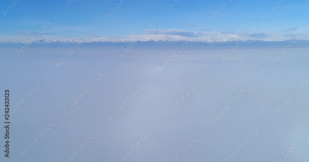 Flying over clouds, rising from the fog to above the fog. European Alps mountain range in the background. Camera moves upwards. Flying over clouds, rising from the fog to above the fog. European Alps mountain range in the background. Camera moves upwards.