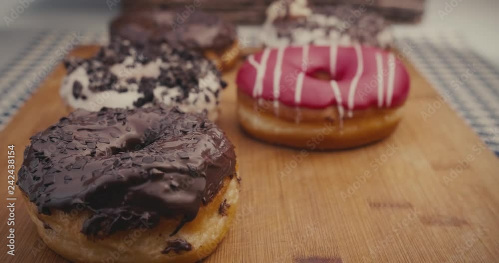 Female hand taking one donut from a plate full of colorful donuts Female hand taking one donut from a plate full of colorful donuts
