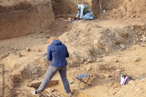 Archaeological excavations. The archaeologists in a digger process, researching the tomb with human bones, drawing the human remains. Real digger process. Outdoors, copy space.