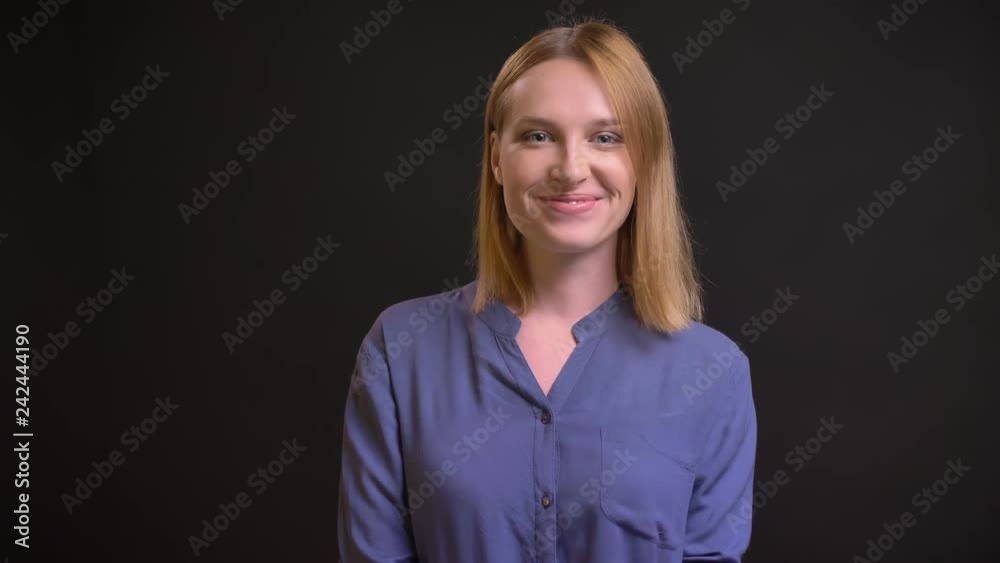 Portrait of formally-dressed woman shyly smiling into camera on black background. Portrait of formally-dressed woman shyly smiling into camera on black background.