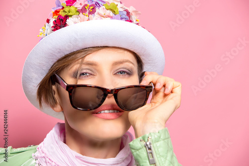 Beautiful spring woman on wearing floral hat, sunglasses, mint jacket over pink background