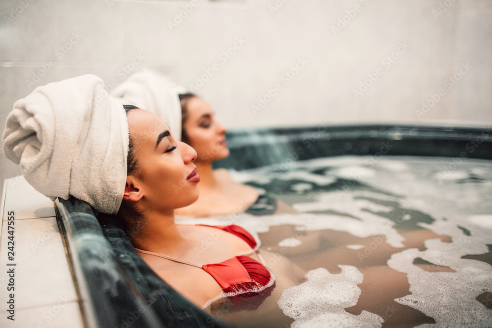 Young asian woman sit in jacuzzi with her european friend. They chill