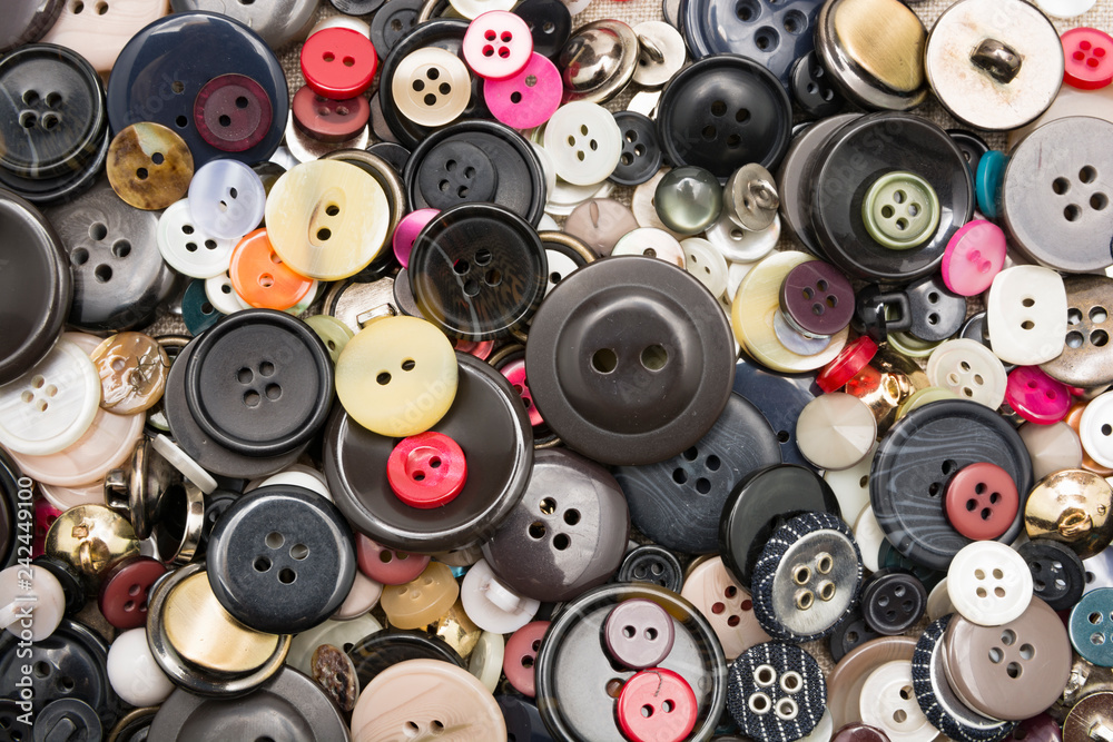 A lot of colorful sewing buttons of different colors of metal and plastic on linen light natural fabric A lot of colorful sewing buttons of different colors of metal and plastic on linen light natural fabric