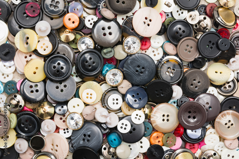 A lot of colorful sewing buttons of different colors of metal and plastic on linen light natural fabric A lot of colorful sewing buttons of different colors of metal and plastic on linen light natural fabric