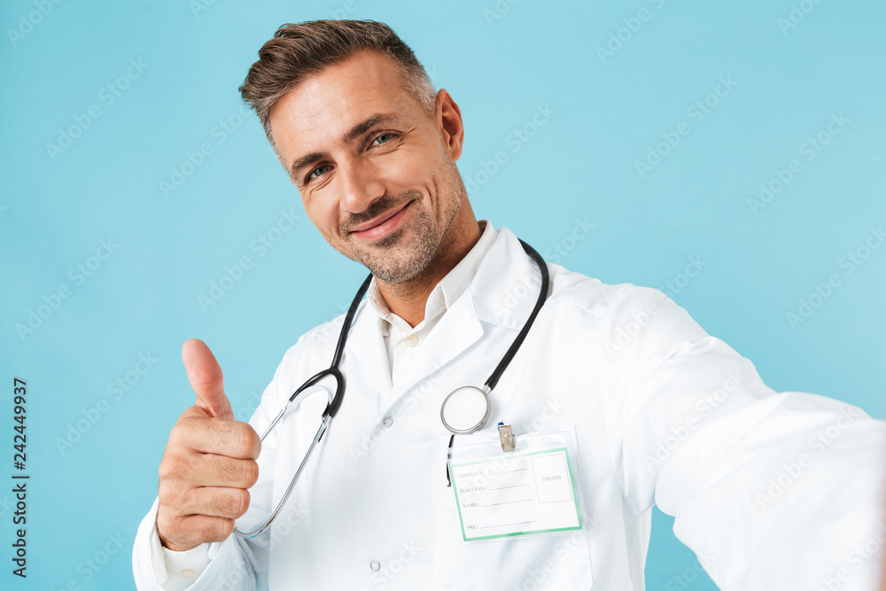 Portrait of happy medical doctor with stethoscope taking selfie photo, while standing isolated over blue background Portrait of happy medical doctor with stethoscope taking selfie photo, while standing isolated over blue background