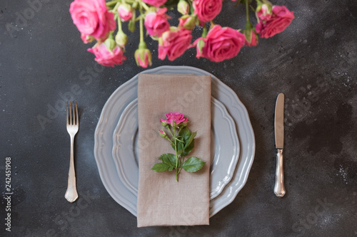 Romantic table setting with pink roses as decor, vintage dishware, silverware, and decorations. Top view.