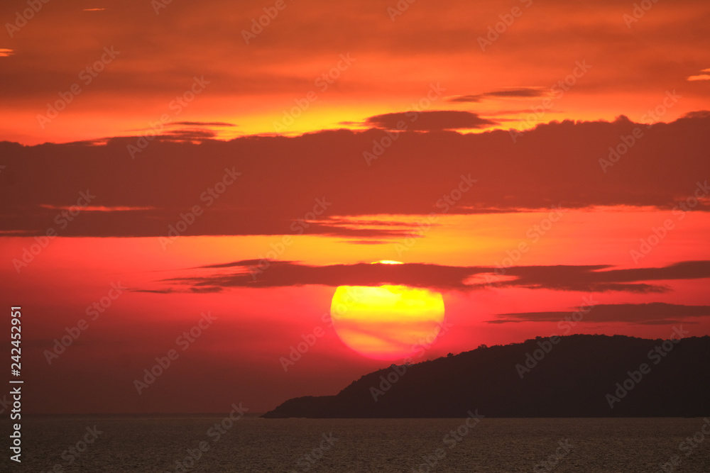 Impressive sunset over the sea and forest island with dramatic orange red fiery sky and dark clouds Impressive sunset over the sea and forest island with dramatic orange red fiery sky and dark clouds