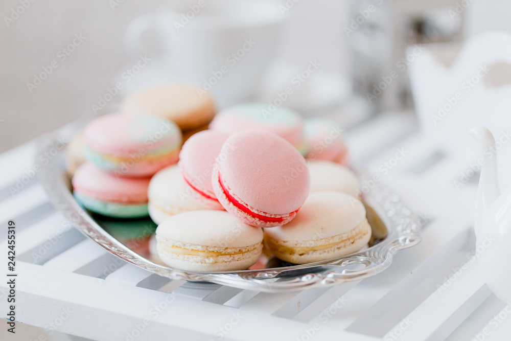 Fototapeta premium Colorful pastel pink, blue, yellow and beige french macaroons on steel tray on white wooden table. Macarons close up.