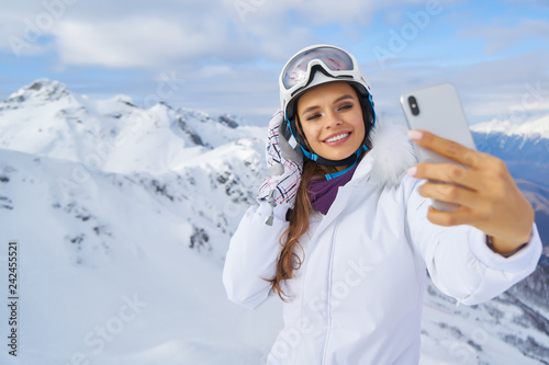 Woman wearing hat make selfie by her phone. Image of young woman wearing hat walking near beach on the street at cold winter day and make selfie by her phone