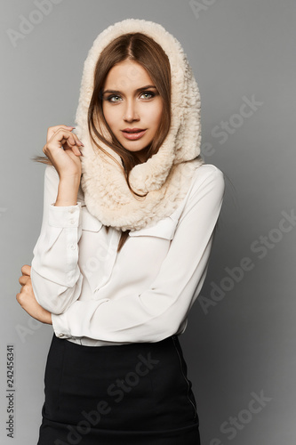 Fashionable and stylish brunette model girl with perfect makeup and blue-grey eyes, in black skirt in white blouse and in the fur hood posing in the studio at grey background, isolated