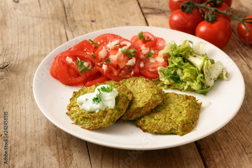 vegetable broccoli pancakes with yoghurt dip, lettuce and tomato, healthy slimming food, white plate on a rustic wooden table