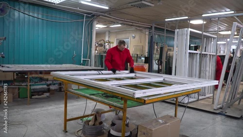Manufacture of plastic windows and doors. Worker fastens the fittings with a screwdriver to the plastic window in the shop for the production of plastic and metal windows and doors. Screwing screws.
