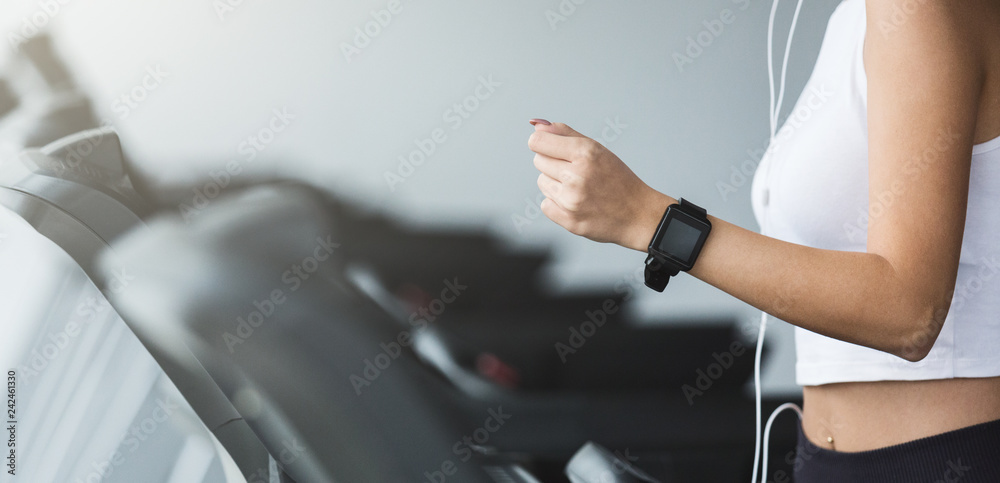 Woman using smartwatch and listening music, running on treadmill