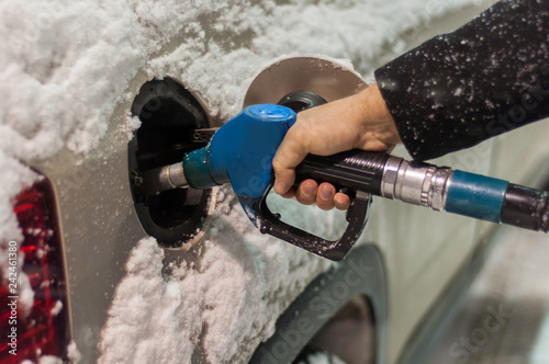 A man refuels his car at a gas station on a snowy winter evening. Hand holding a blue refueling gun.