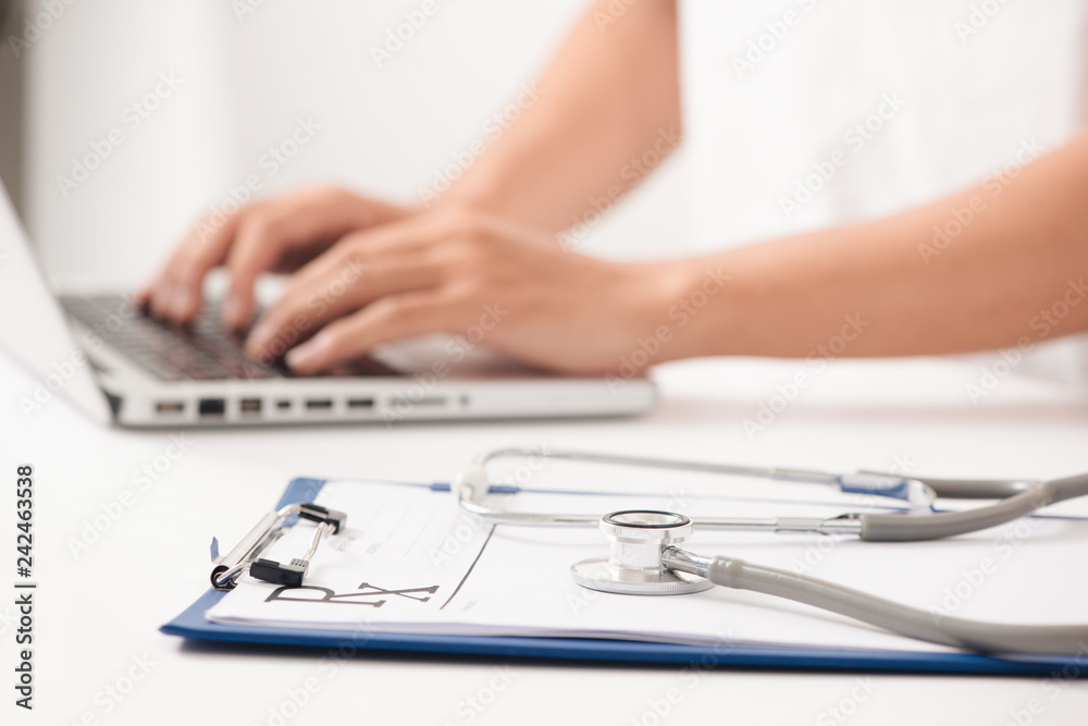 Close-up of a female doctor typing on laptop computer, sitting at the table in the hospital Close-up of a female doctor typing on laptop computer, sitting at the table in the hospital