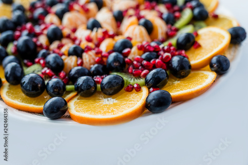 Fruit dessert. Orange, grapes, pomegranate on a white plate. Festive table.