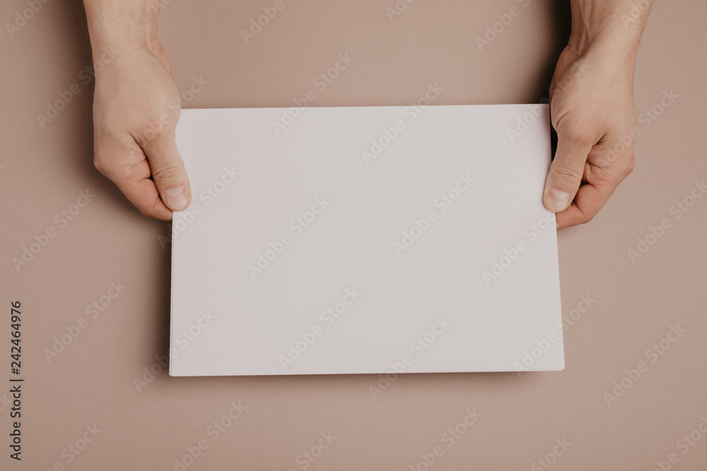 Hands holding paper blank a4 size on grey background. Hands holding paper blank a4 size on grey background.
