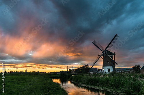Windmill in Gouda, Holland along a canal with a colorful sunset.  Scenic view of a typical dutch landscape with a beautiful colored sky.