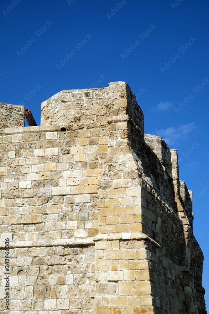 Top section of antique castle wall from old sandy limestone and the cannon on the top under clear blue sky ion sunny day