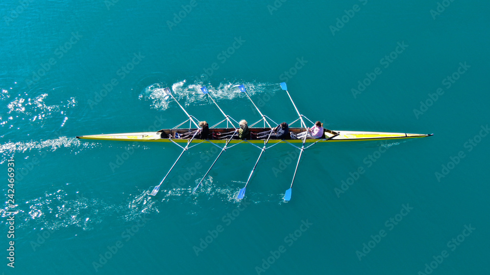 Aerial drone bird's eye top down view of sport canoe operated by team of young men in open ocean emerald sea