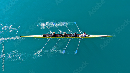 Aerial drone bird's eye top down view of sport canoe operated by team of young men in open ocean emerald sea