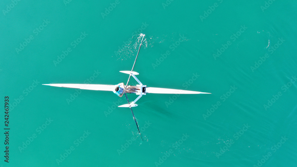 Aerial drone bird's eye view of sport canoe operated by young fit man in turquoise clear waters Aerial drone bird's eye view of sport canoe operated by young fit man in turquoise clear waters