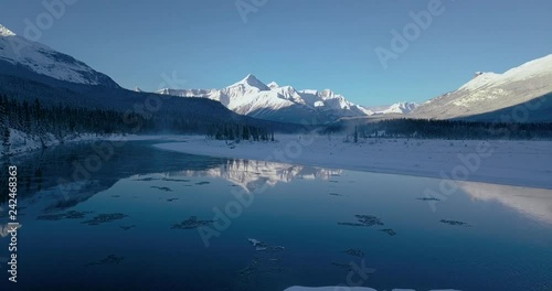 Aerial footage of flying over the river in the mountains during the winter while it was beautiful sunrise Canadian Rockies Banff, Alberta, Canada.