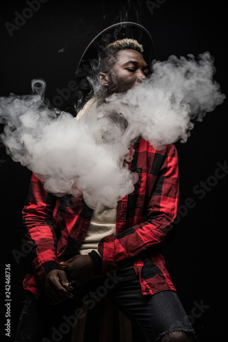 Young african man on a black background holding an electronic cigarette, vaping device, mod, e-cig isolated on black background