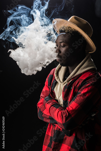 The African man smoke an electronic cigarette on the dark background