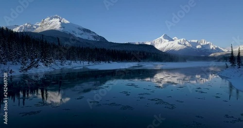 Aerial footage of flying over the river in the mountains during the winter while it was beautiful sunrise Canadian Rockies Banff, Alberta, Canada.