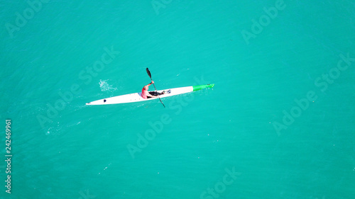 Aerial drone bird's eye view of sport canoe operated by young fit man in emerald clear waters