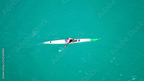 Aerial drone bird's eye view of sport canoe operated by young fit man in emerald clear waters