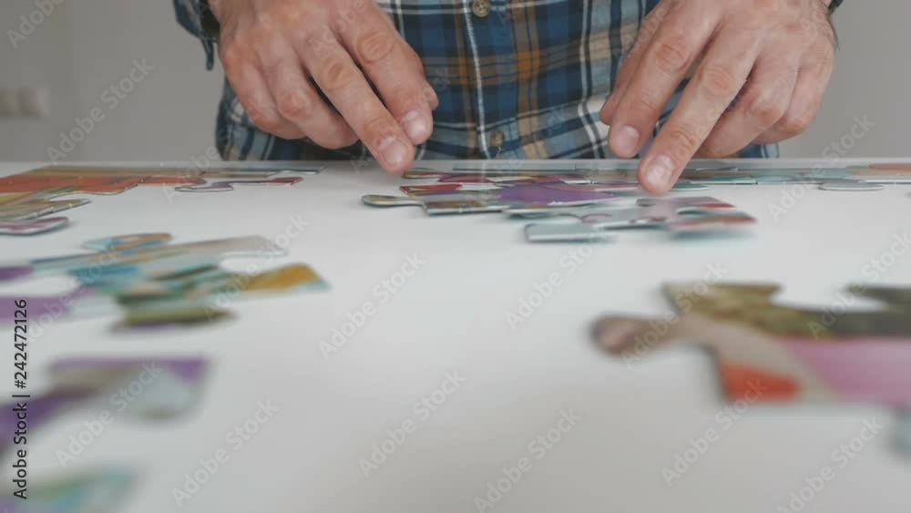 A man collects large puzzles on the table in the apartment A man collects large puzzles on the table in the apartment