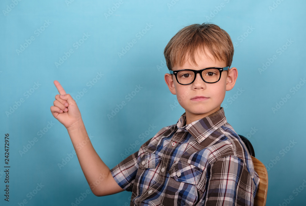 a charming European boy with glasses points his finger at the empty space. blue background a charming European boy with glasses points his finger at the empty space. blue background