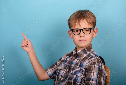 a charming European boy with glasses points his finger at the empty space. blue background