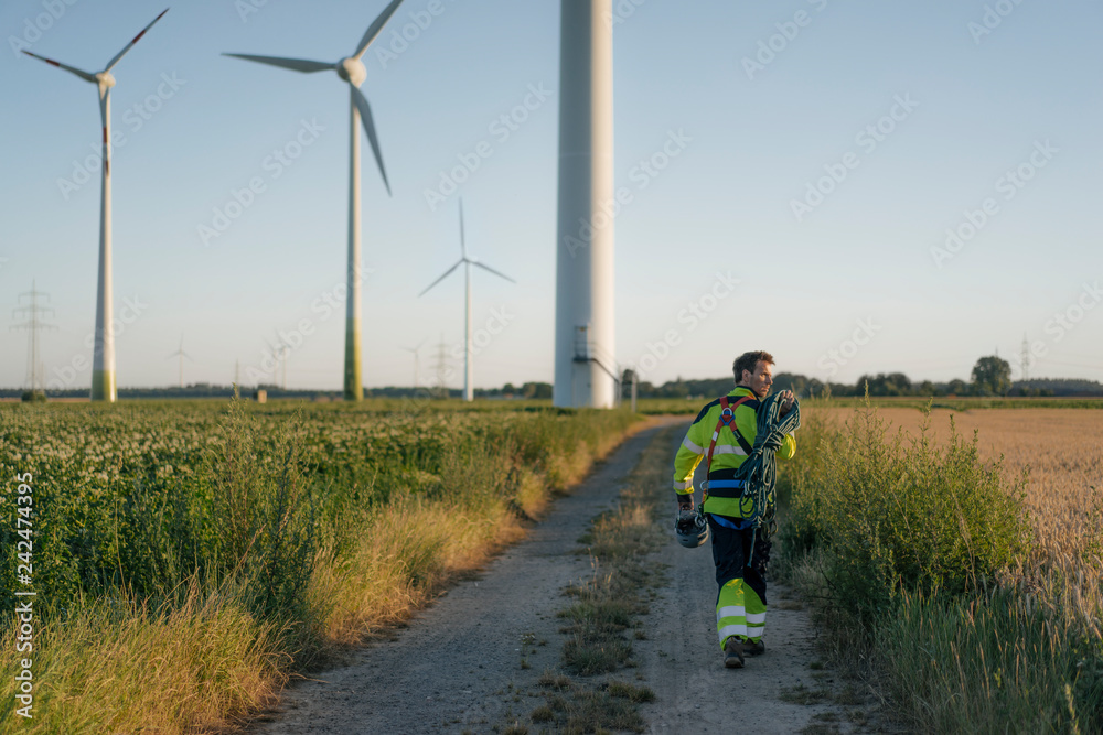 Technician walking on field path at a wind farm with climbing equipment Technician walking on field path at a wind farm with climbing equipment