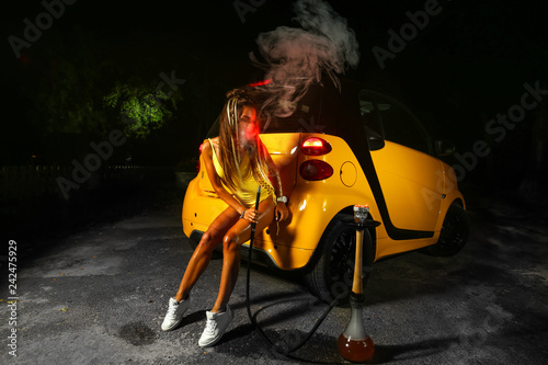 young sexy girl smoke hookah in yellow swimming suit in night close to yellow car 