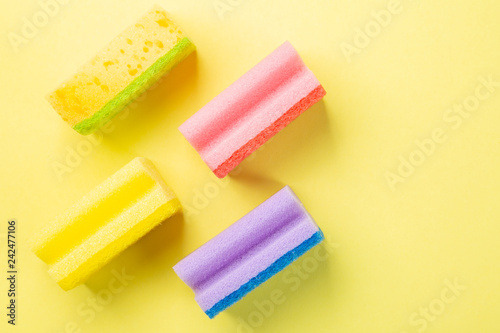Cleaning concept - pastel colour sponges on yellow background, top view