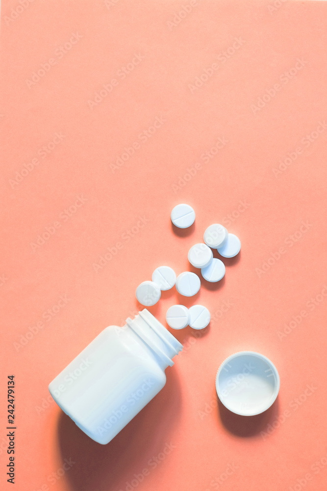 white pills scattered on a pink background. pills spilled out of the bottle. copy space for text
