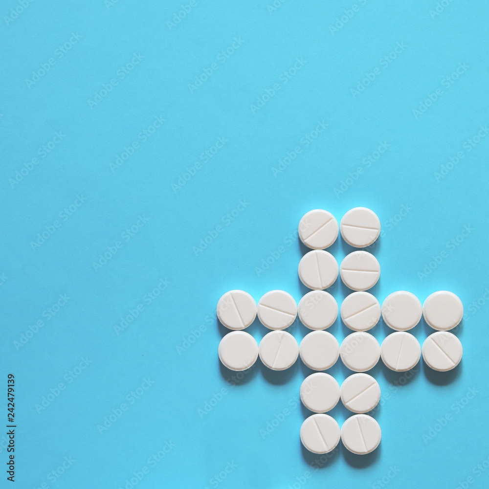white pills laid out in the shape of a cross on a blue background. copy space for text