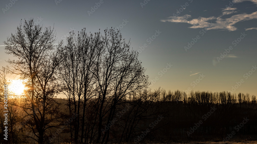 Fototapeta premium Sun flare shining over a blue dusk sky and foggy landscape