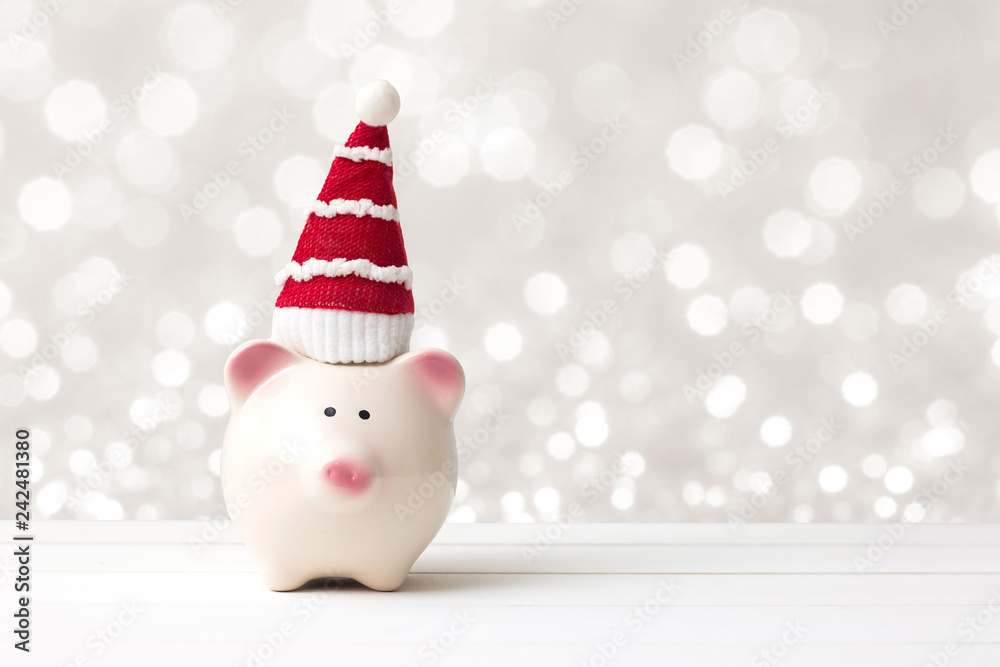 Piggy bank and santa claus hat over white wooden table abstract bokeh light background with copy space. Saving and christmas holiday concept.