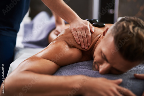 Masseur hands massaging client shoulder while he lying on massage table