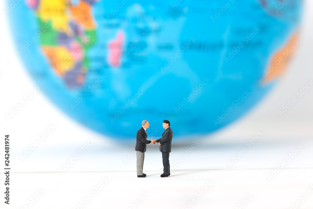 Miniature businessmen shaking hands on blurred global or world background. Concept of partnership. Business successful. Miniature businessmen shaking hands on blurred global or world background. Concept of partnership. Business successful.