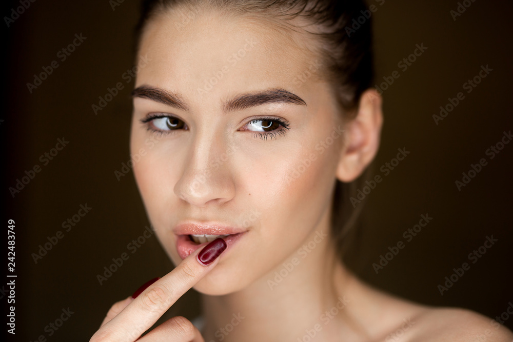 Portrait of young brown-haired girl with natural makeup holding her fingers on her face Portrait of young brown-haired girl with natural makeup holding her fingers on her face