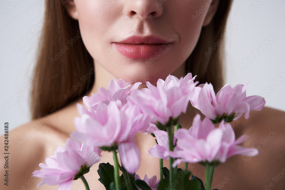 Young woman with plump lips holding beautiful pink flowers